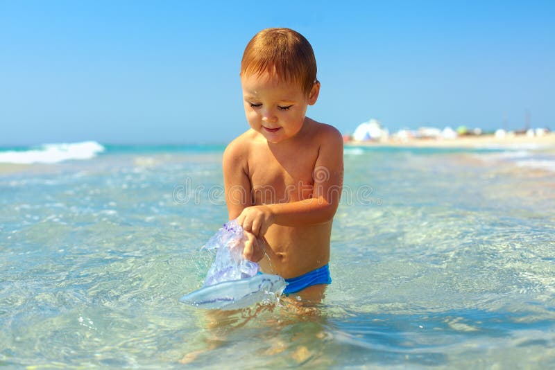 Curious baby boy catches jellyfish in the sea stock photography