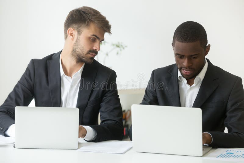 Zvedavý kaukazský samec podnikateľ pozerá na obrazovka z americký kolega zaneprázdnený pracovné na prenosný počítač, pracovník pozrel na súper počítač, bytia chytrý, mazaný, mazaný.