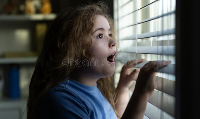 Curious child peeking through the window blinds. Kid observing outdoors with a curious expression. Child leaning toward the window stock photos