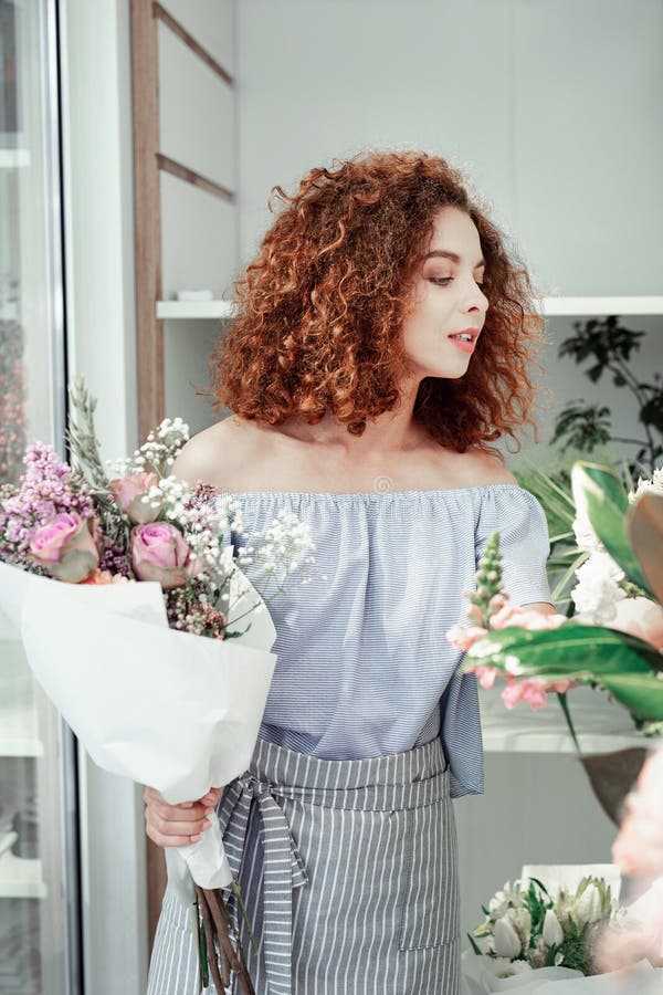 Curious good-looking red-haired woman looking on different flowers in stock royalty free stock photos