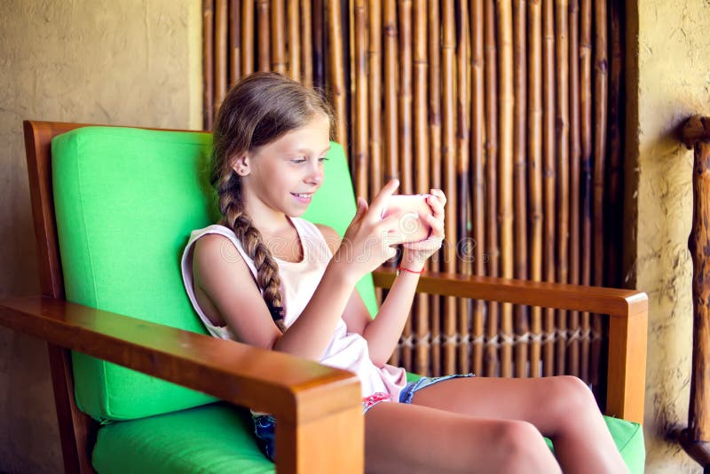 Curious little girl playing games on her mobile phone indoors. stock photo Curious little girl playing games on her mobile phone indoors. stock photo