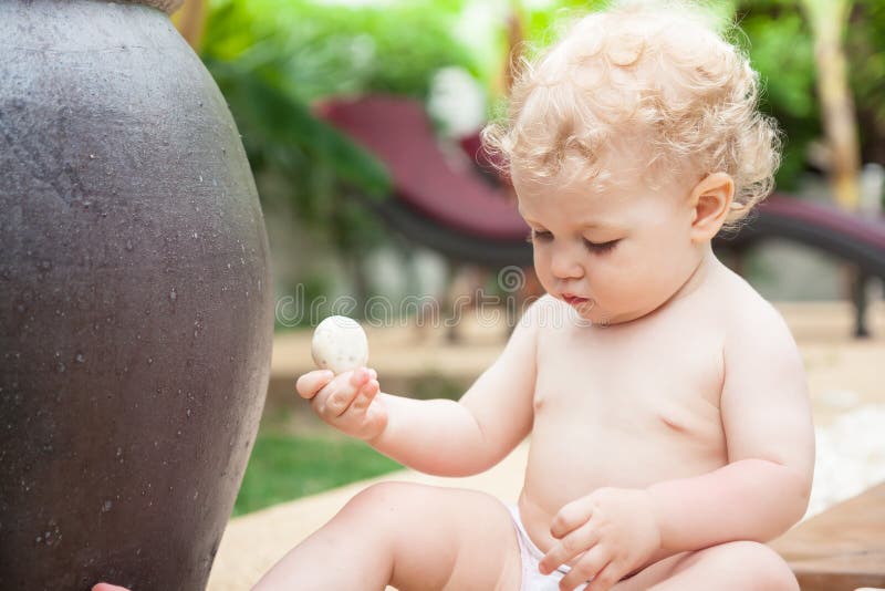 Curious zen baby girl playing with stone in tropical zen garden royalty free stock images