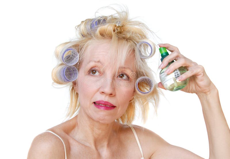 A blonde woman with lavender curlers in her hair, spraying product onto .....