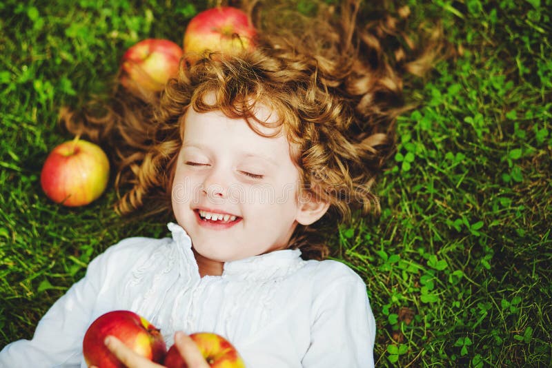 Curly girl lies on the grass with apple and smiling.