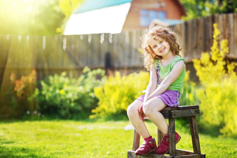 Curly girl sits on a chair in the yard of a country house.