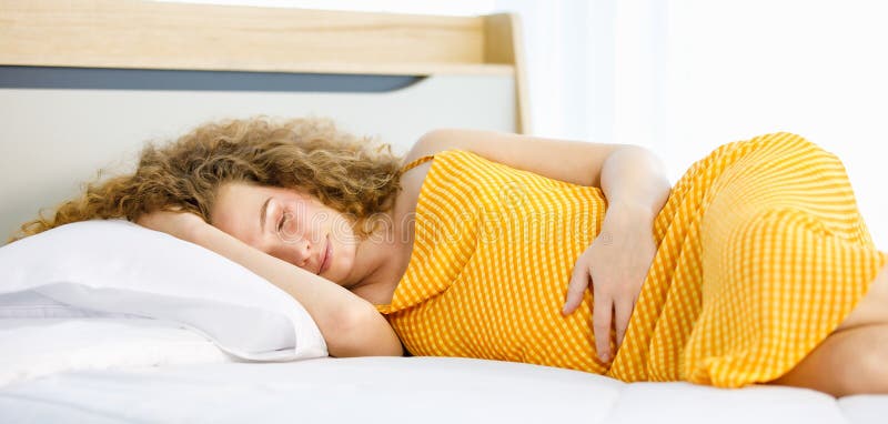 Curly hairstyle young tired exhausted sleepy Caucasian pregnancy mother in orange maternity long dress cloth lay down holding hand