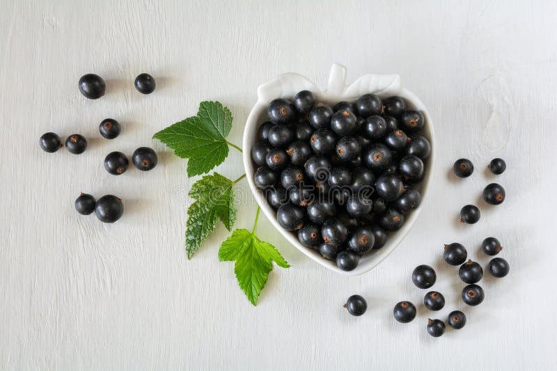 Currant berries in a white berry-shaped bowl on a white wooden background royalty free stock photography