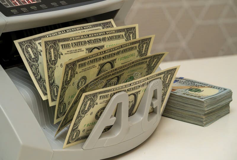 Currency counting machine processes several dollar bills efficiently. A currency counting machine is sorting multiple one-dollar bills while a stack of neatly organized banknotes is placed beside it.
