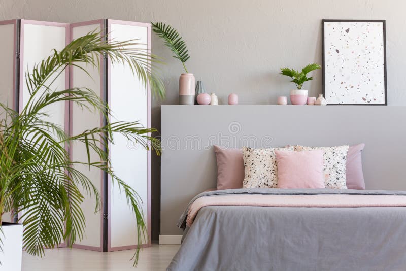 Cuscini rosa sul letto grigio nell'interno pastello della camera da letto con la palma ed il manifesto su bedhead Foto reale immagini stock