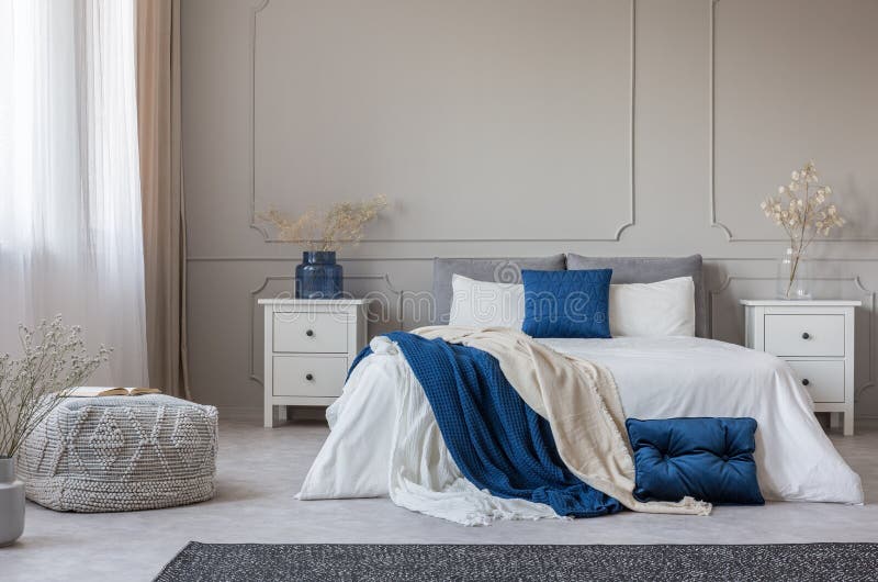Cuscino blu e coperta su letto bianco in camera spaziosa all'interno, spazio vuoto sulla parete grigia immagine stock