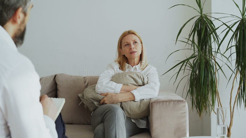Cuscino turbato della tenuta della donna adulta e parlare dei suoi problemi con lo psicanalista maschio nel suo ufficio