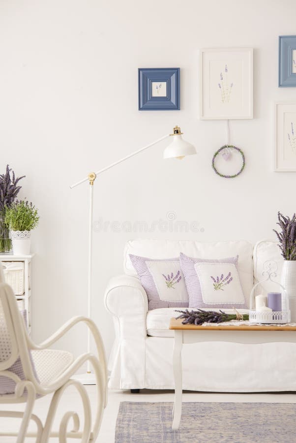 Cushions on white settee in living room interior with posters and wooden table. Real photo concept