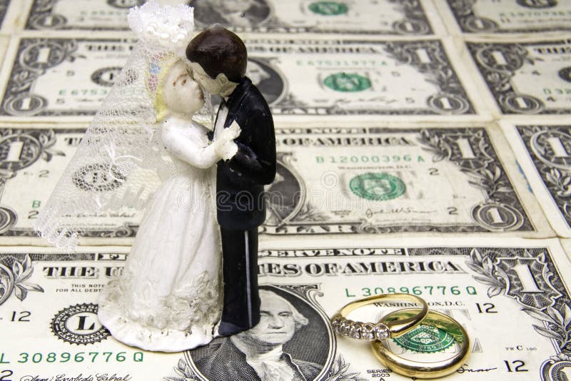 Bride and groom ornament with marriage bands on top of a sheet of one dollar bills. Bride and groom ornament with marriage bands on top of a sheet of one dollar bills.