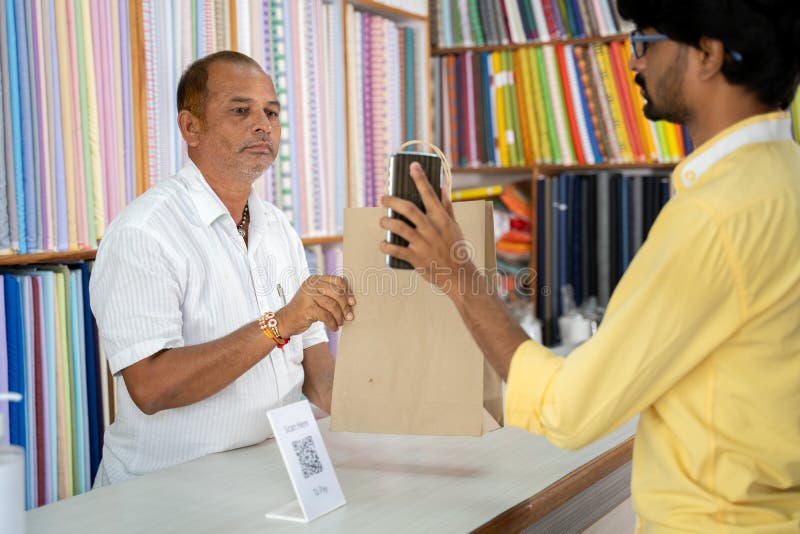Customer using digital payment method scan to pay at cloth store to send money and shoing to shopkeeper - concept of digital or contactless payment, e-transfer, technology and lifestyle.