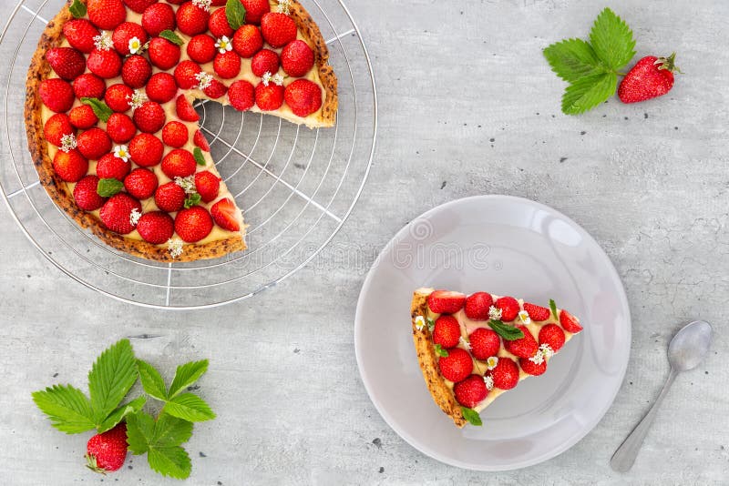 Cut French strawberry tart with wild strawberry leaves and flowers on a cooling rack with a slice in a plate on a grey background stock photo Cut French strawberry tart with wild strawberry leaves and flowers on a cooling rack with a slice in a plate on a grey background stock photo