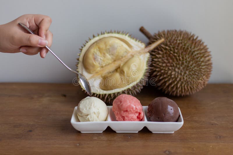 Metal spoon reaching out to ice cream with a cut open durian fruit on a wooden board with a triple scoop ice cream on a plate royalty free stock photo