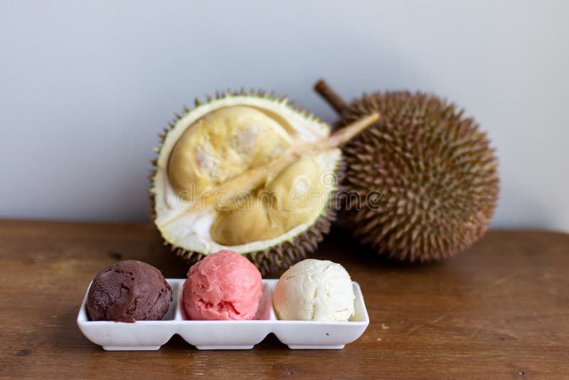 Cut open durian fruit on a wooden board with a triple scoop ice cream on a plate on a closer look royalty free stock photography.