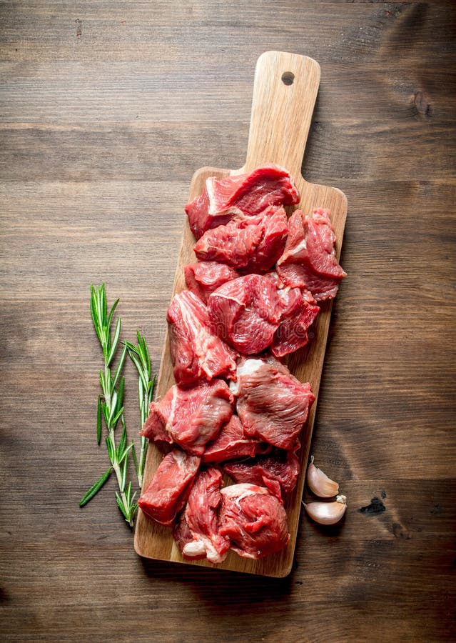 Cut raw beef on a wooden cutting Board with rosemary and garlic