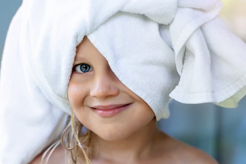 Cute adorable caucasian little blond girl wearing white towel on we head after shower or bathing at bathroom. Portrait