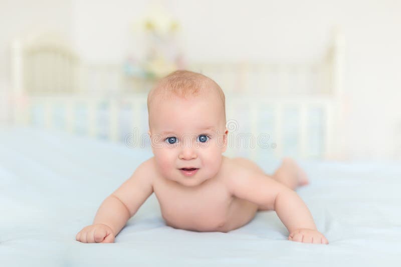 Cute adorable caucasian little 5 month old infant baby boy lying on tummy at nursery bed room having fun playing and smiling.