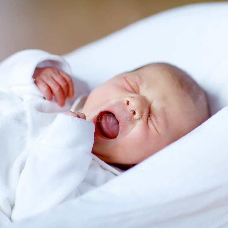 Cute adorable newborn baby crying in white bed. New born child, little girl laying in bed. Family, new life, childhood