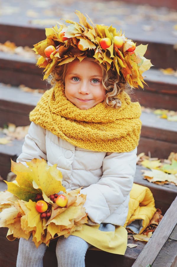 Cute adorable toddler girl portrait with bouquet of autumn leaves and wreath walking outdoor in park