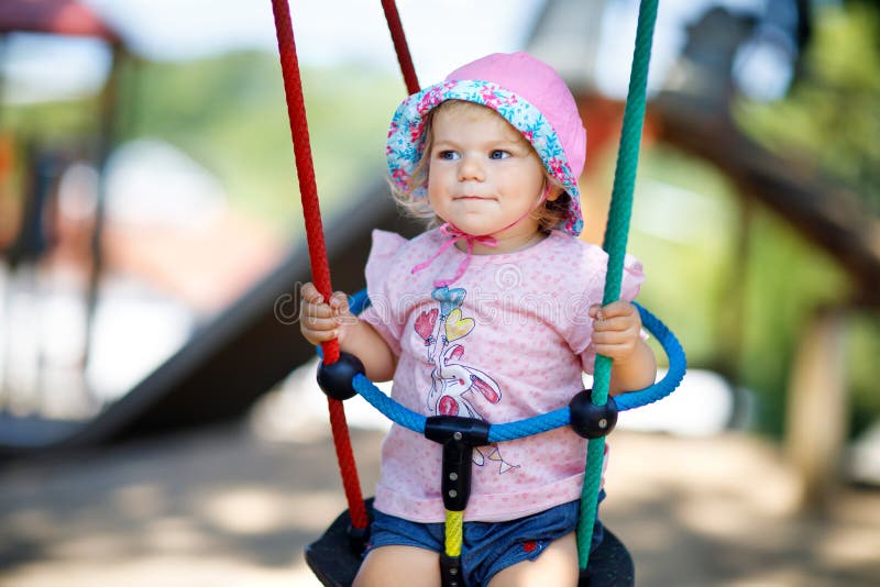Cute adorable toddler girl swinging on outdoor playground. Happy smiling baby child sitting in chain swing. Active baby royalty free stock photo Cute adorable toddler girl swinging on outdoor playground. Happy smiling baby child sitting in chain swing. Active baby royalty free stock photo