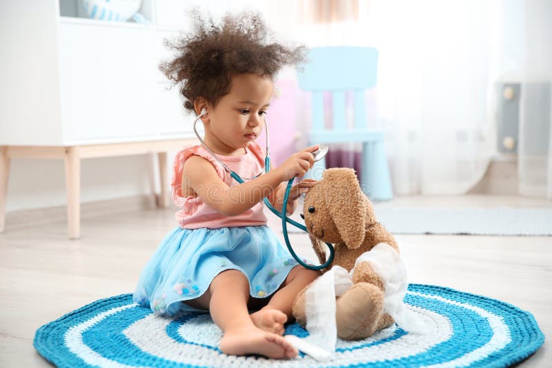 Cute African American child imagining herself as doctor while playing with stethoscope and toy bunny