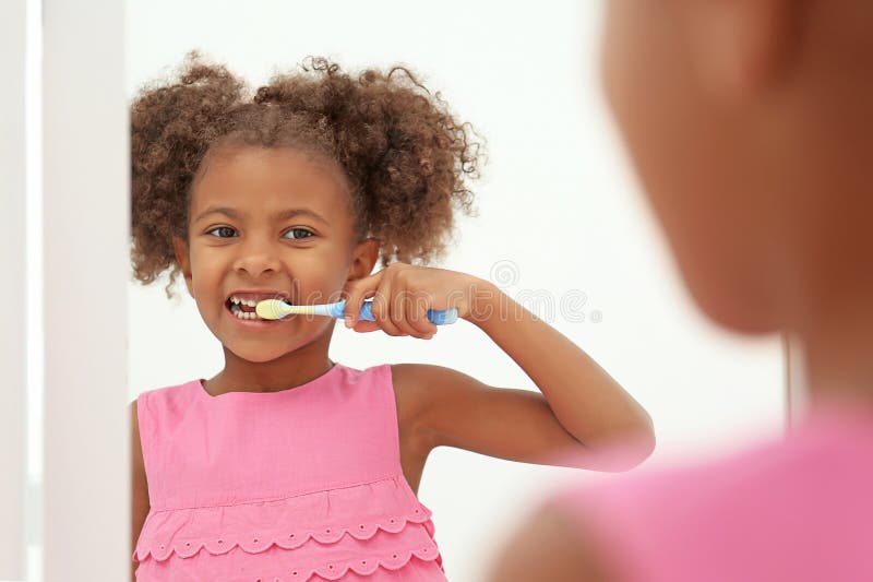 Cute African American girl brushing teeth and looking in mirror in bathroom royalty free stock image Cute African American girl brushing teeth and looking in mirror in bathroom royalty free stock image