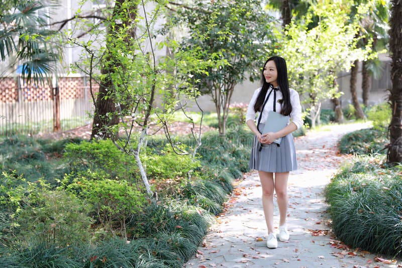 Cute Asian Chinese pretty girl wear student suit in school hold a book walking