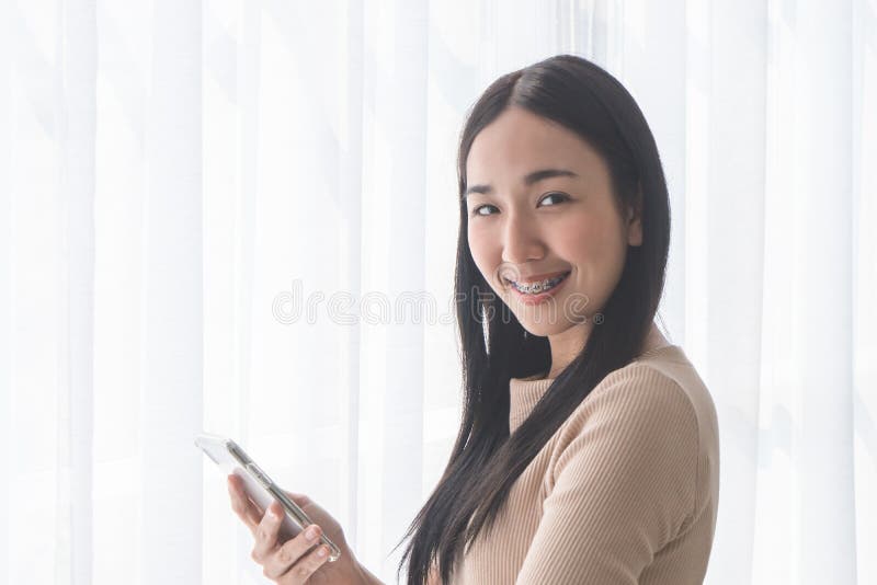 Cute Asian girl using mobile phone by morning windows stock photo Cute Asian girl using mobile phone by morning windows stock photo