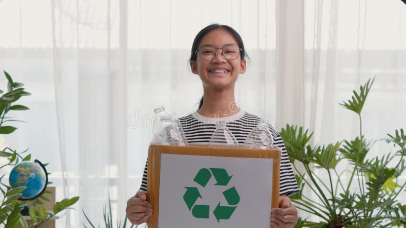 A cute Asian girl carries a paper box full of plastic water bottles. Children sort out trash for recycling. Cultivate the learning royalty free stock images