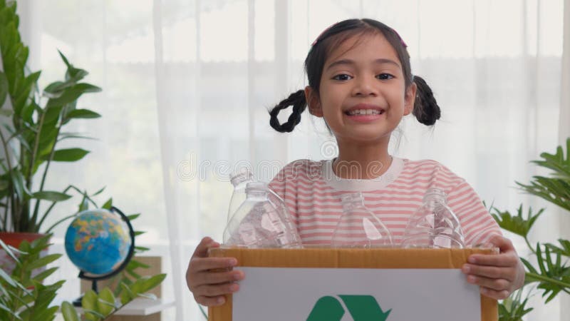 A cute Asian girl carries a paper box full of plastic water bottles. Children sort out trash for recycling. Cultivate the learning stock image