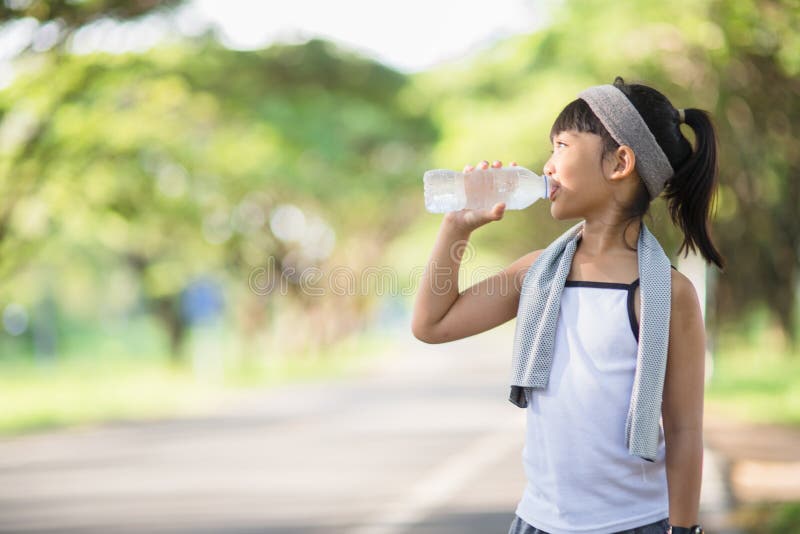 Cute asian girl drinks water from a bottle outdoors  with sunllight