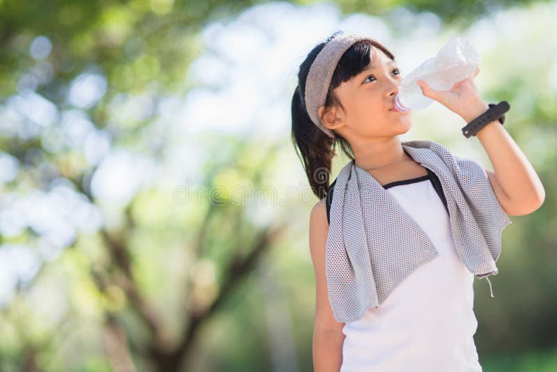 Cute asian girl drinks water from a bottle outdoors  with sunllight.