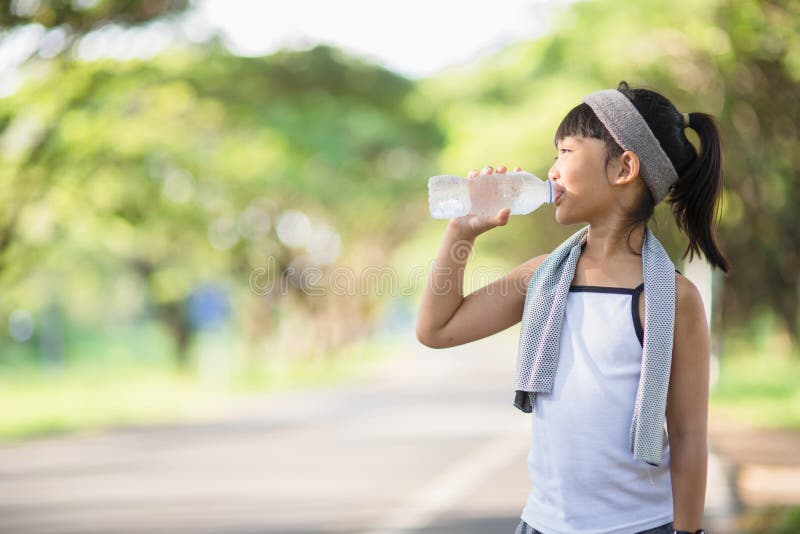 Cute asian girl drinks water from a bottle outdoors  with sunllight.