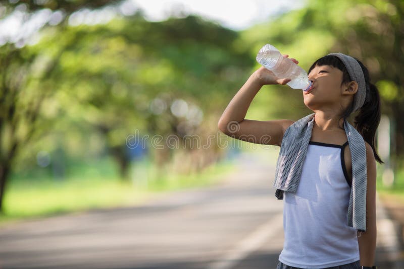 Cute asian girl drinks water from a bottle outdoors  with sunllight