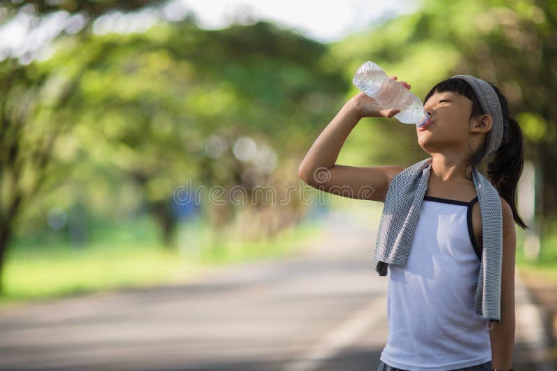 Cute asian girl drinks water from a bottle outdoors  with sunllight.