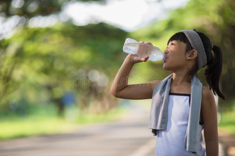 Cute asian girl drinks water from a bottle outdoors  with sunllight.