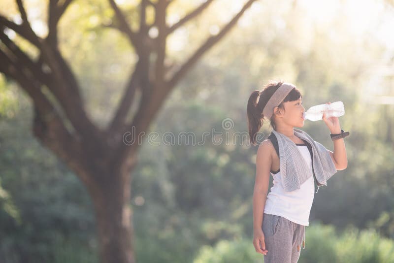 Cute asian girl drinks water from a bottle outdoors  with sunllight.