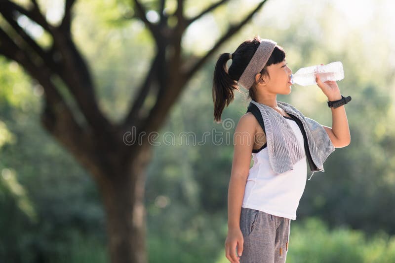 Cute asian girl drinks water from a bottle outdoors  with sunllight.