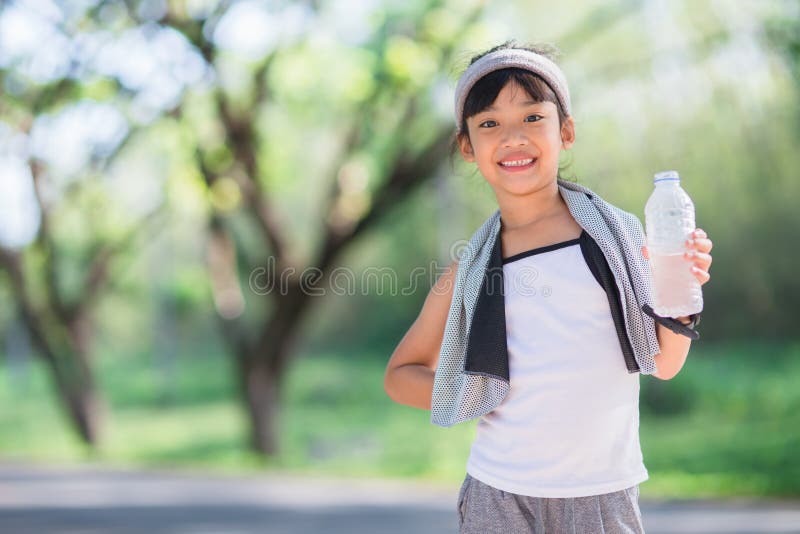 Cute asian girl drinks water from a bottle outdoors  with sunllight.