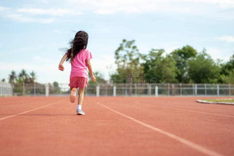 Cute Asian kid girl dressed in pink sportswear, aged 4 to 6, are having fun playing in the stadium. Running on an outdoor court is