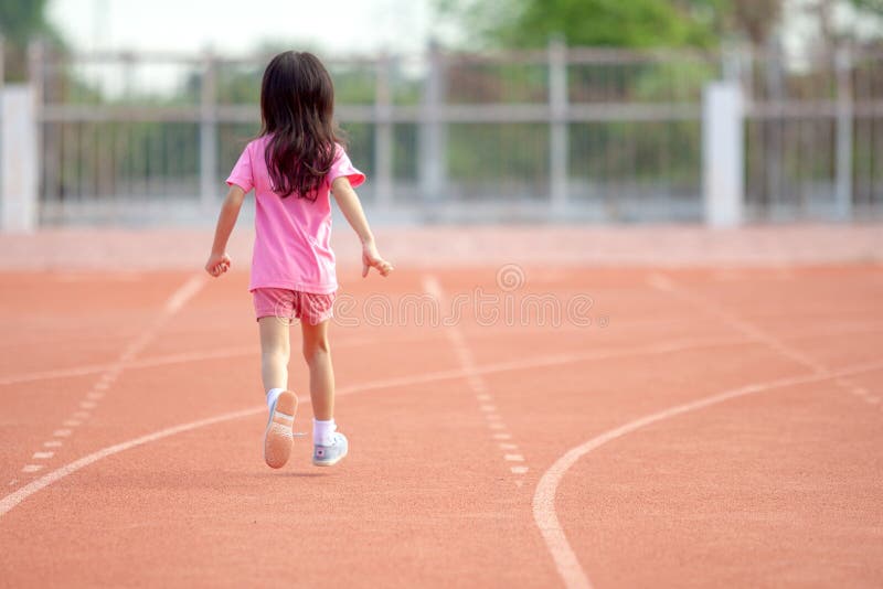 Cute Asian kid girl dressed in pink sportswear, aged 4 to 6, are having fun playing in the stadium. Running on an outdoor court is