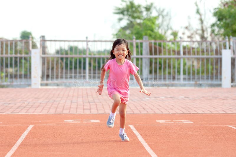 Cute Asian kid girl dressed in pink sportswear, aged 4 to 6, are having fun playing in the stadium. Running on an outdoor court is