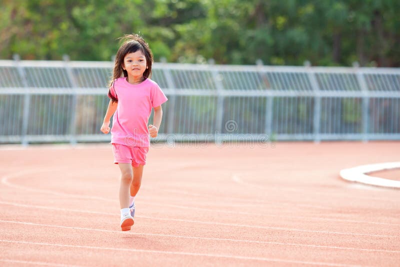 Cute Asian kid girl dressed in pink sportswear, aged 4 to 6, are having fun playing in the stadium. Running on an outdoor court is