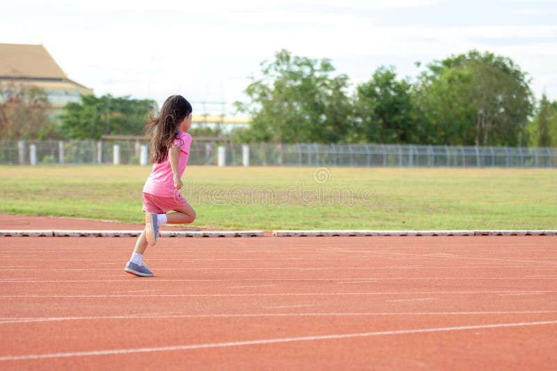 Cute Asian kid girl dressed in pink sportswear, aged 4 to 6, are having fun playing in the stadium. Running on an outdoor court is