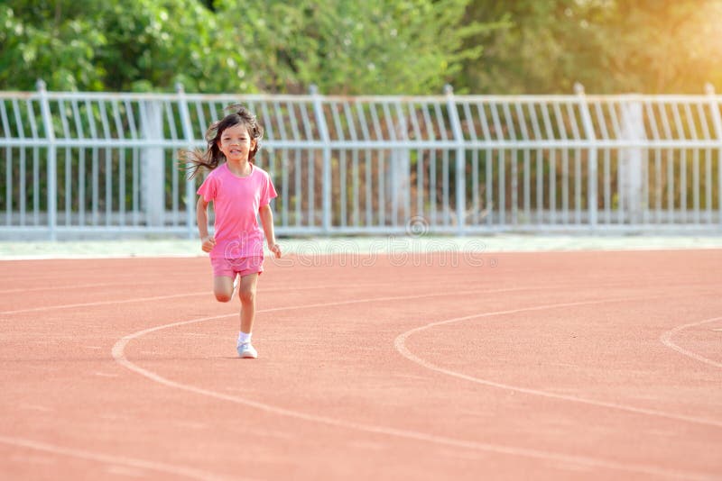 Cute Asian kid girl dressed in pink sportswear, aged 4 to 6, are having fun playing in the stadium. Running on an outdoor court is