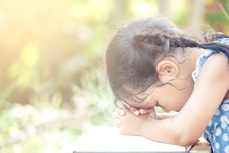 Cute asian little child girl praying with folded her hand on a Holy Bible for faith,spirituality and religion concept in vintage color tone