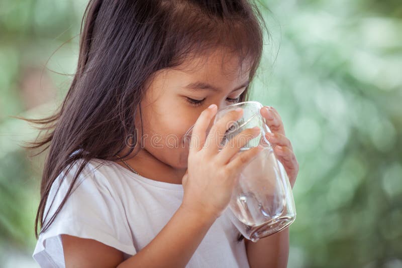 Cute asian little girl drinking fresh water from glass